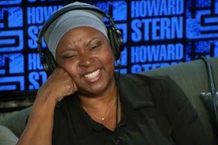 Robin Quivers resting her hand on her cheek with a headphone on her head during Howard Stern show