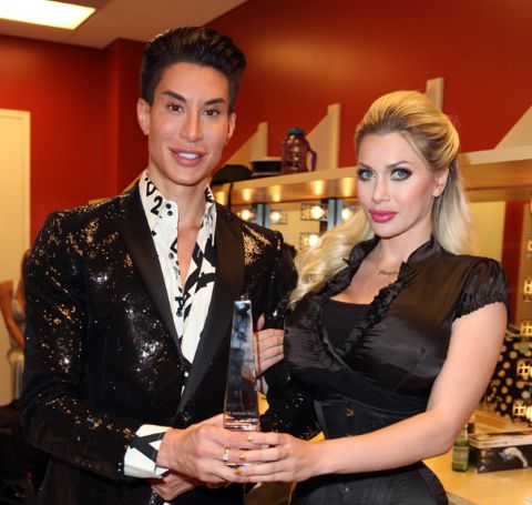 Pixee Fox in black dress, blonde hair poses with Justin Jedlica, on a black shiny coat and white shirt.