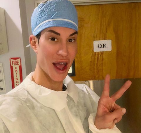 Justin Jedlica in doctor's gaun covering his head shows victory sign. 