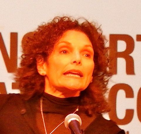 Mary Elizabeth Mastrantonio  in a black dress speaking with mike in front.