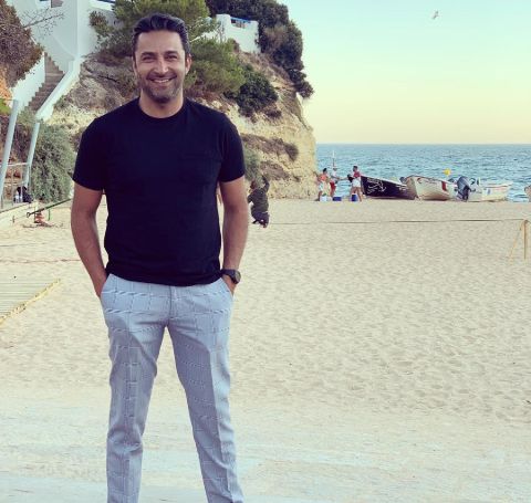 Pej Vahdat in a black t-shirt and white pant at a beach.