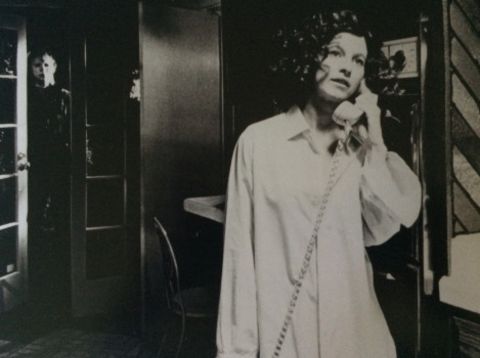 Nancy Kyes in a white dress holding a phone. 