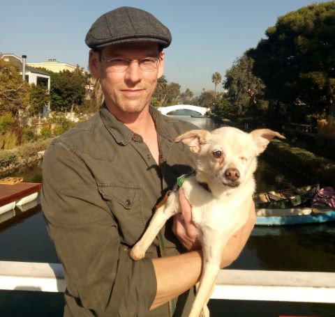 A man in a green shirt and a cap holding a dog.