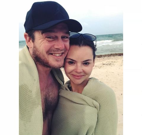 Eline Powell wrapped around a towel at a beach besides her fiance Lee Lenox. 