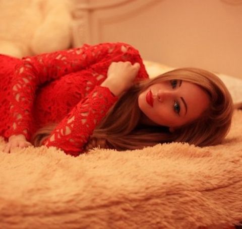 Alina Kovalevskaya in a red dress lying on a bed.