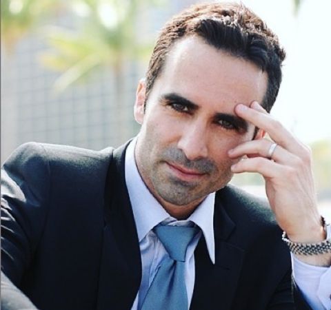 Nestor Carbonell in a black suit and blue tie.
