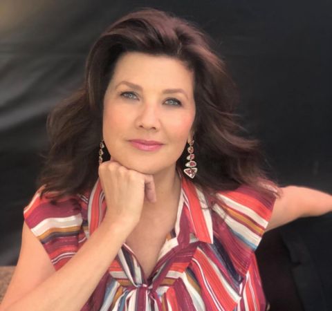 Daphne Zuniga in a red top poses for a photo.