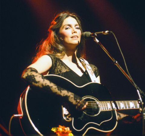 Emmylou Harris singing at a concert with her guitar.