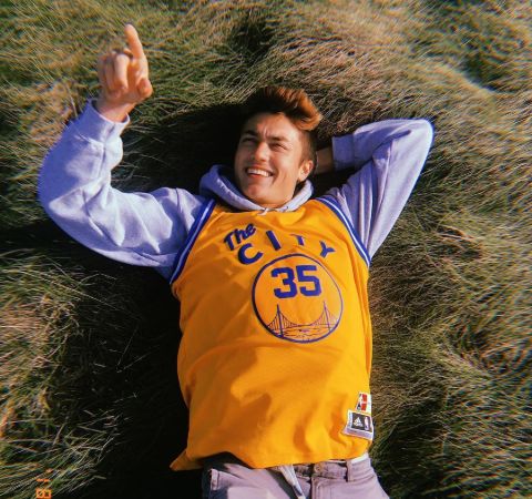 Kelly Wakasa in a yellow t-shirt lying at a meadow.
