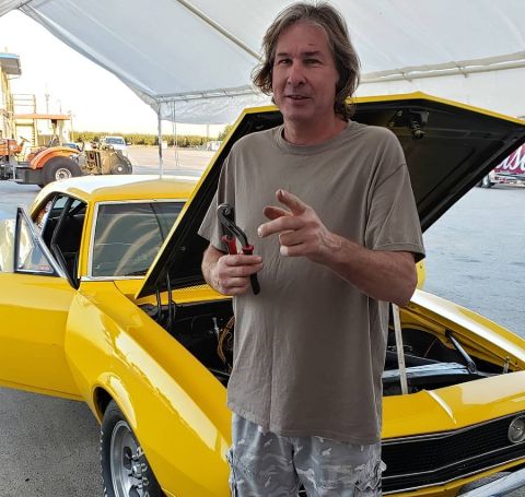 Steve Dulcich poses in front of a yellow car.
