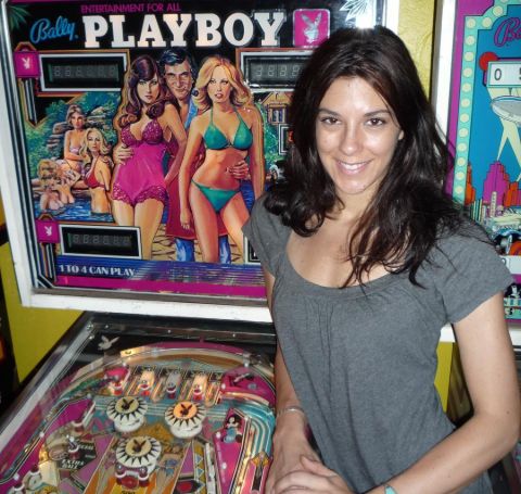 Jenna Morasca in a grey outfit poses before a playboy magazine stand.