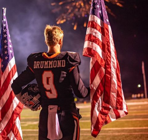 Bryce Drummond in the jersey of Pawhuska High School holds the national flag.