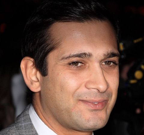 Jimi Mistry in a grey suit poses for a picture.