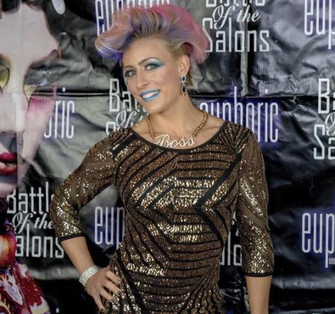 Angelique Kenney in a black-golden dress and pink hair poses at a photoshoot in an event.