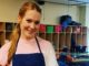 Darby Stanchfield in a pink t-shirt and blue apron poses for a picture.