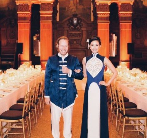 Rachel Kum in a white-blue dress poses alongside husband Alex Lloyd.
