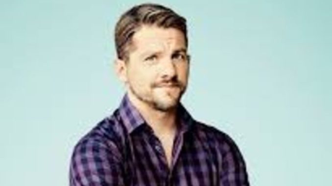 Zachary Knighton in a pink shirt poses for a picture.