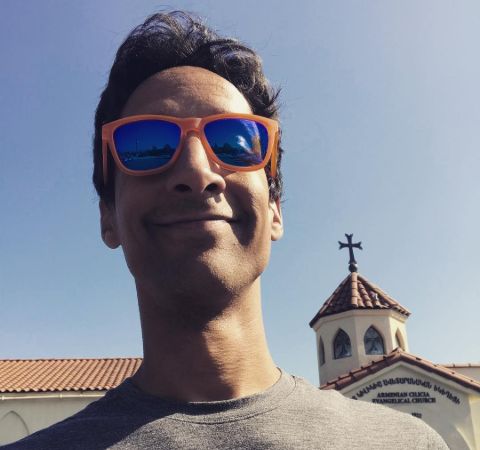 Danny Pudi in a grey t-shirt poses for a selfie.