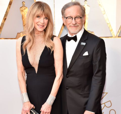 Kate Capshaw in black dress poses alongside Steven Spielberg in a tux.