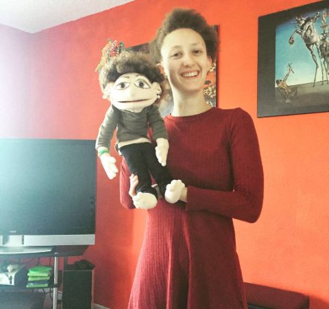 Maya Eshet in a red dress poses with a doll.